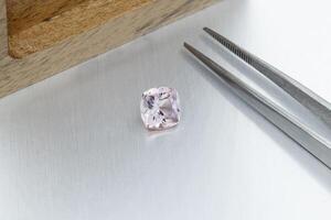 macro mineral faceted stone Morganite with tweezers on a gray background photo