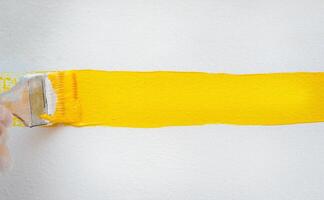 A brush with yellow paint leaves a mark on a wall photo