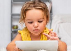 The child lies on the floor and uses a tablet photo