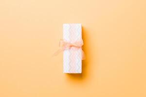 wrapped Christmas or other holiday handmade present in paper with orange ribbon on orange background. Present box, decoration of gift on colored table, top view with copy space photo