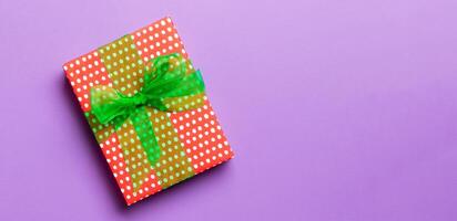 wrapped Christmas or other holiday handmade present in paper with green ribbon on purple background. Present box, decoration of gift on colored table, top view with copy space photo