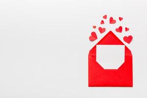 Red paper envelope with empty white card and heart on colored background. top view valentines day concept photo