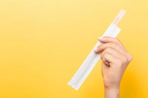 Woman's hand holding chopsticks in a pack on yellow background. Chinese food concept with empty space for your design photo