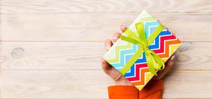 Woman arms holding gift box with colored ribbon on yellow rustic wooden table background, top view and copy space for you design photo