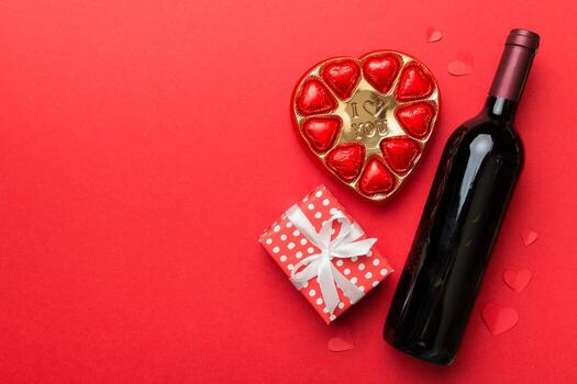 Bottle of red wine on colored background for Valentine Day with gift and chocolate. Heart shaped with gift box of chocolates top view with copy space photo