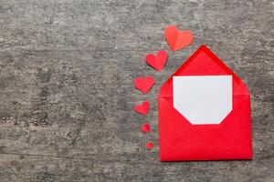 Red paper envelope with empty white card and heart on colored background. top view valentines day concept photo