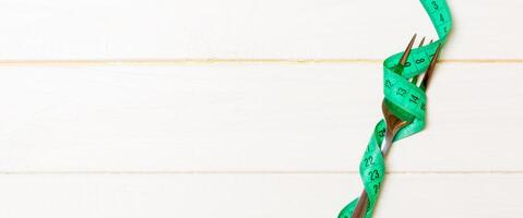 Top view of obesity concept with fork wrapped in measuring tape on wooden background with space for your creative ideas photo