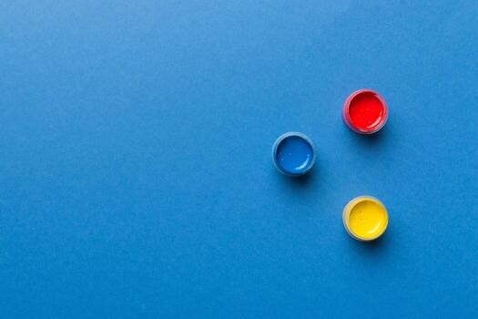 jars with gouache of different colors on Colored background. hobby painting. Top view with empty space. workplace for creativity. home teaching concept drawing photo