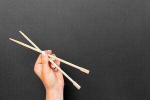 Female hand holding chopsticks on black background. Sushi concept with empty space for your idea photo