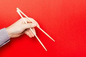 Wooden chopsticks holded with male hands on red background. Ready for eating concepts with empty space photo