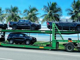 Car Carrier Truck Transporting Black SUVs and Double Cabins along a Scenic Tropical Highway photo