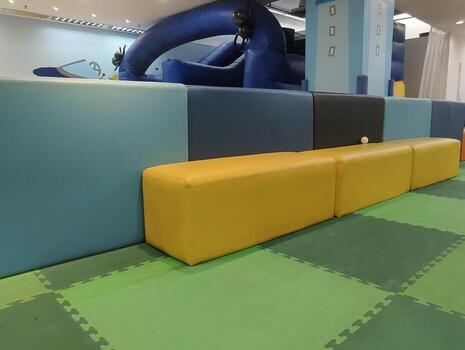A modern playroom featuring soft green floor mats and yellow cushioned seating, providing a safe and comfortable space for children to play photo