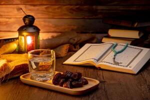 Many Date Palms are on bowls, plates, a cup of water, and the Quran, islamic style lamps on wooden tables, to wait for the time of Iftar, with the concept of ramadan Muslims around the world. photo