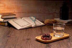 Many Date Palms are on bowls, plates, a cup of water, and the Quran, islamic style lamps on wooden tables, to wait for the time of Iftar, with the concept of ramadan Muslims around the world. photo