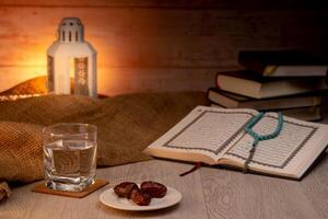 Many Date Palms are on bowls, plates, a cup of water, and the Quran, islamic style lamps on wooden tables, to wait for the time of Iftar, with the concept of ramadan Muslims around the world. photo