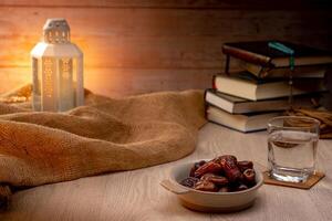 Many Date Palms are on bowls, plates, a cup of water, and the Quran, islamic style lamps on wooden tables, to wait for the time of Iftar, with the concept of ramadan Muslims around the world. photo