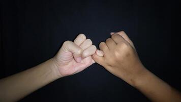 Two hands with a gesture showing the promise of the little finger.Isolated on black background photo