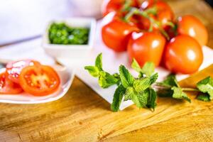 Red fresh tomatoes with mint and basil on wooden table over bokeh background photo