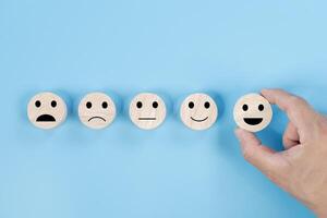 Hand holding smile face symbol on wooden cube blocks on blue background. Customer service evaluation photo