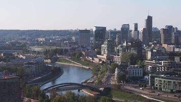 Aerial view of Vilnius, Lithuania, featuring the Neris River, bridges, modern and historical architecture, and green spaces against distant hills. video