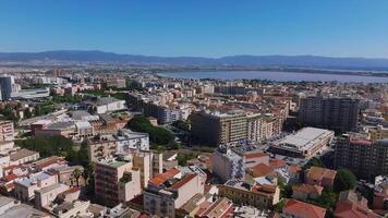 Cagliari's mix of modern and traditional architecture is seen from above, with colorful buildings and the Gulf of Cagliari framed by distant mountains. video
