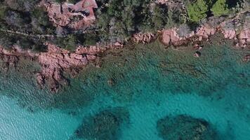 Aerial view of Sardinia's coast with turquoise waters, rocky shorelines, a wooden dock, and lush greenery creating a serene atmosphere. video