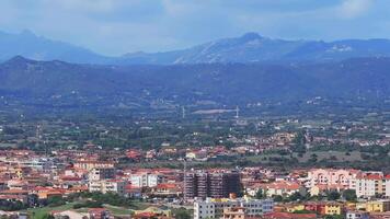 An aerial view captures a Sardinian town with colorful buildings, red tiled roofs, and lush green hills, showcasing Mediterranean architecture. video