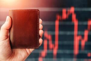 Hand holding wallet, financial chart in background photo