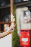 Hand holding Soft Serve Vanilla Ice Cream Cone with blurred cafe background. Selective focus. photo