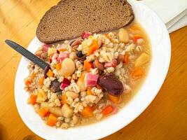 Hearty barley and bean soup with rustic bread on wooden table photo