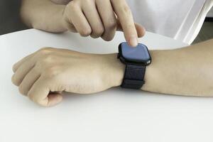 Young man using electronic smartwatch on his hand. Wearables with digital touchscreen and mobile app technology. Person using wristwatch for business and work. Device with touch interface. photo