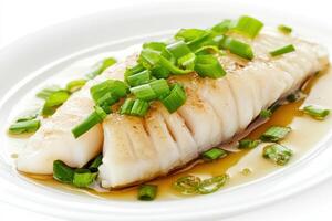 Steamed fish fillet garnished with green onions in a savory sauce on a white plate. photo