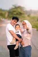 A young family that looks happy and laughing out loud with mother, father and baby boy. mother pointed at the camera while laughing happily. photo taken vertically. photo atmosphere in nature.