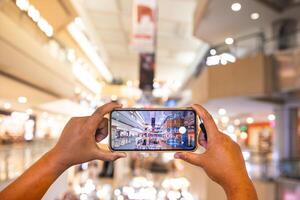 a man's hand taking pictures of objects in the mall. the man is seen using his cellphone to take pictures of objects around him. the portrait results are very clear and good. photo