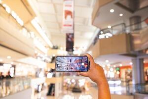 a man's hand taking pictures of objects in the mall. the man is seen using his cellphone to take pictures of objects around him. the portrait results are very clear and good. photo