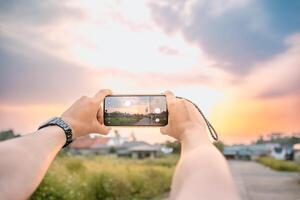a man who is taking photos of the scenery. he uses a cell phone camera. set in a bright natural atmosphere in the afternoon.
