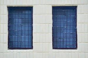 Two windows, bricked up with grey brick and covered with bars, on a tiled wall photo