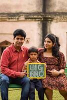 Indian couple posing for maternity baby shoot with their 5 year old kid. The couple is posing in a lawn with green grass and the woman is flaunting her baby bump in Lodhi Garden in New Delhi, India photo