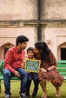 Indian couple posing for maternity baby shoot with their 5 year old kid. The couple is posing in a lawn with green grass and the woman is flaunting her baby bump in Lodhi Garden in New Delhi, India photo