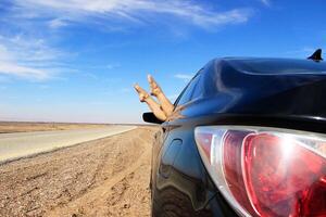 A relaxing road trip through the desert, with legs playfully hanging out of a car window against the backdrop of the vast open road and clear blue sky photo