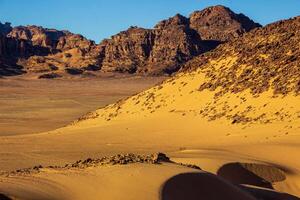 A stunning view of the sand dunes and unique rock formations in the Jordanian desert, capturing the dramatic landscape under the clear blue sky photo