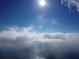 Aerial view. The drone flies over foggy and fluffy clouds. Blue sky sun and sea fog. Abstract aerial nature summer ocean sunset sea and sky background. Vacation, travel and holiday concept photo