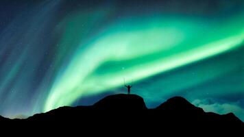 Aurora borealis with starry glowing over hiker standing on summit mountain in the night photo