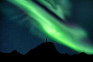 Aurora borealis with starry glowing over hiker standing on summit mountain in the night photo