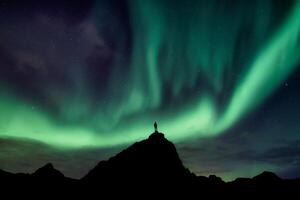 Aurora borealis with starry glowing over hiker standing on summit mountain in the night photo