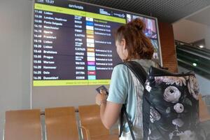 The girl goes on a flight in the airport, holds a passport and tickets in her hands, looks at the gate number in search of her plane, the woman goes on a trip with a backpack. photo