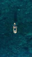 Woman floating on transparent kayak in blue sea. Drone top down view, vertical screen video