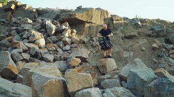 a traveler with a backpack in shorts and a black t-shirt is sitting on a large rock and examining a beautiful landscape around himself video