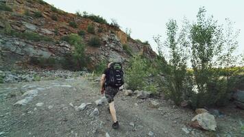 traveler in comfortable clothes and in running shoes is walking at the edge of a river near the rocks on the background of a beautiful view in the summer video