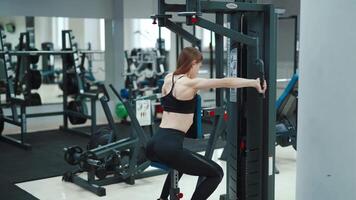 A woman with a sporty figure is sitting and doing an exercise to strengthen the back muscles in the gym. Blurred Background video